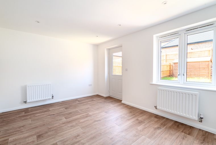A room with laminate flooring, a radiator, a door, and a window.