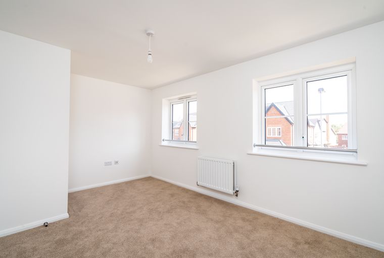 A room with carpet, windows, and a radiator.
