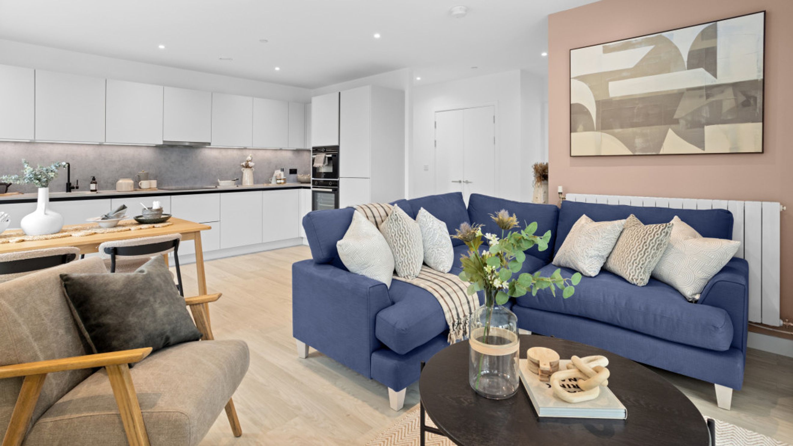 A living room and kitchen area with a blue sectional sofa, dining table, and modern kitchen cabinets.