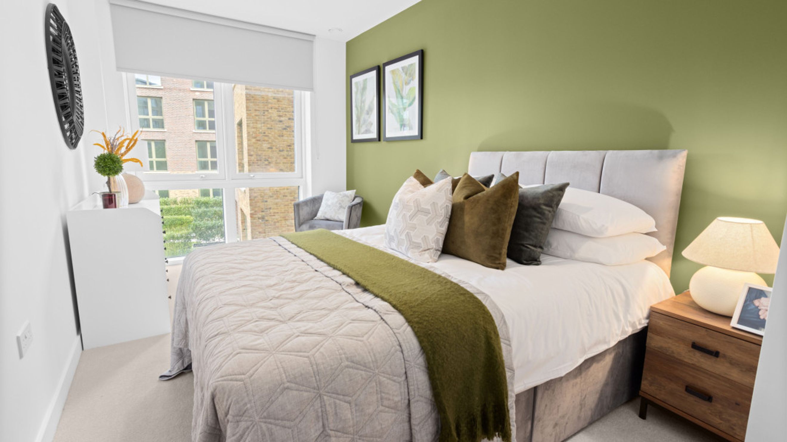 A bedroom with a bed, pillows, a throw blanket, and a nightstand with a lamp.