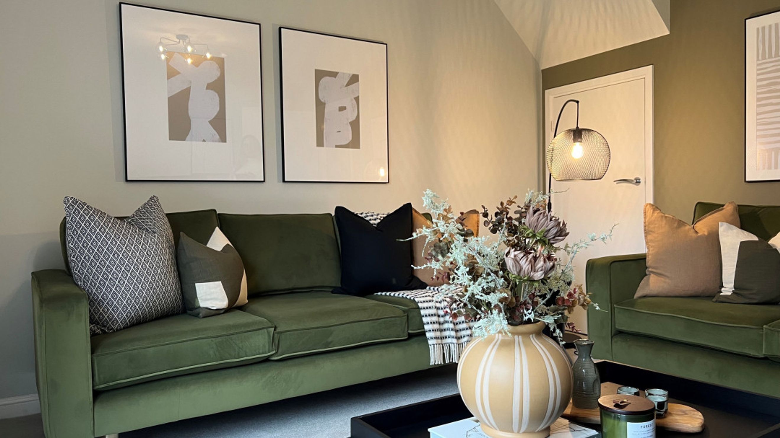 A living room with green sofas, throw pillows, abstract art, and a floor lamp.