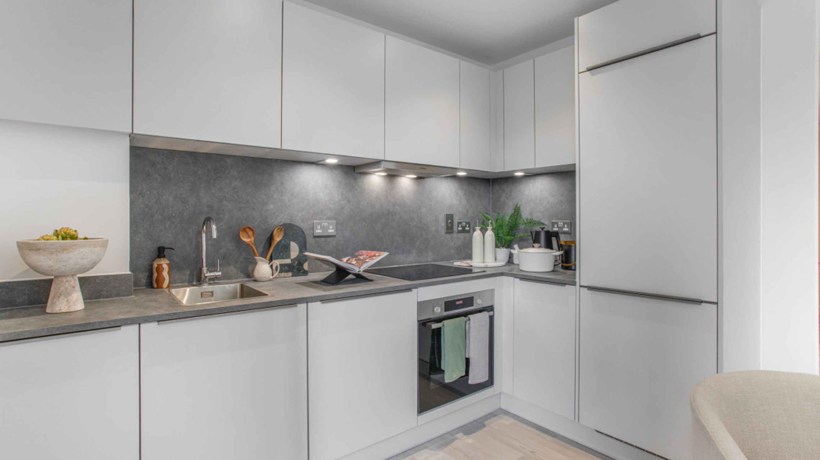 A modern kitchen with white cabinets, a dark grey backsplash, a sink, and an oven.