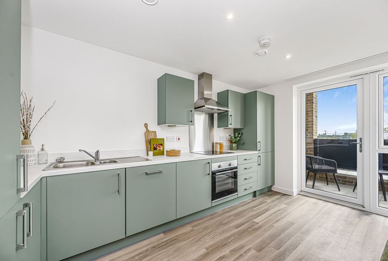 A modern kitchen with sage green cabinets, a double sink, and an oven, next to a glass door leading to a patio.
