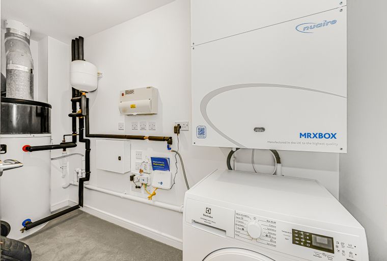 A utility room with a washing machine, ventilation unit, and plumbing.