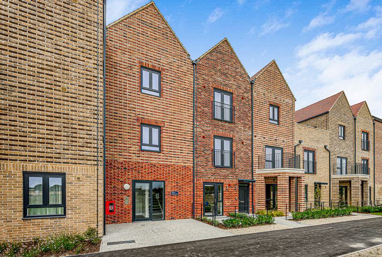 A row of modern brick townhouses with dark-framed windows and balconies under a blue sky.