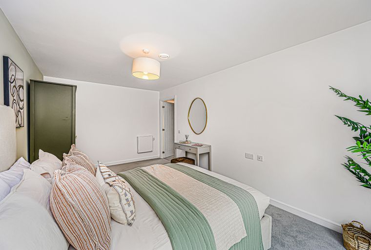 A bedroom with a bed, pillows, a vanity, a mirror, and a wardrobe.