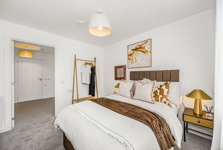 A bedroom with a bed, pillows, a throw blanket, a garment rack, and a bedside lamp.