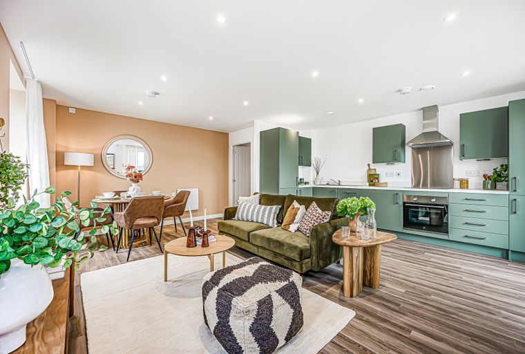 A living room and kitchen area with a green sofa, dining table, and green kitchen cabinets.