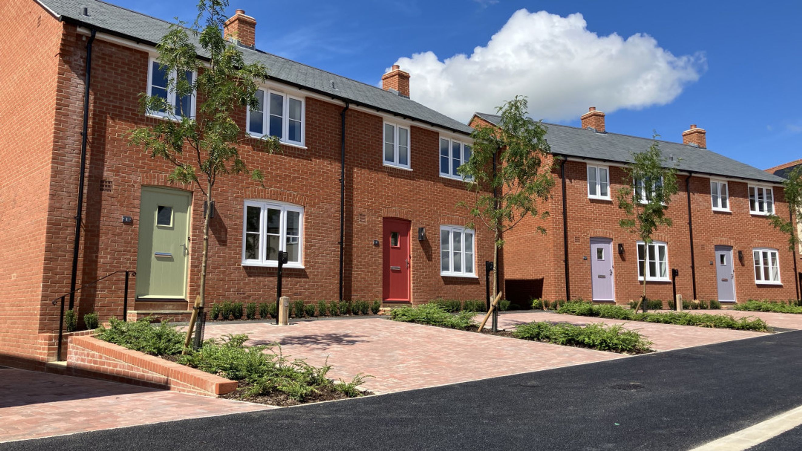 A row of red brick townhouses with white windows and colorful front doors.