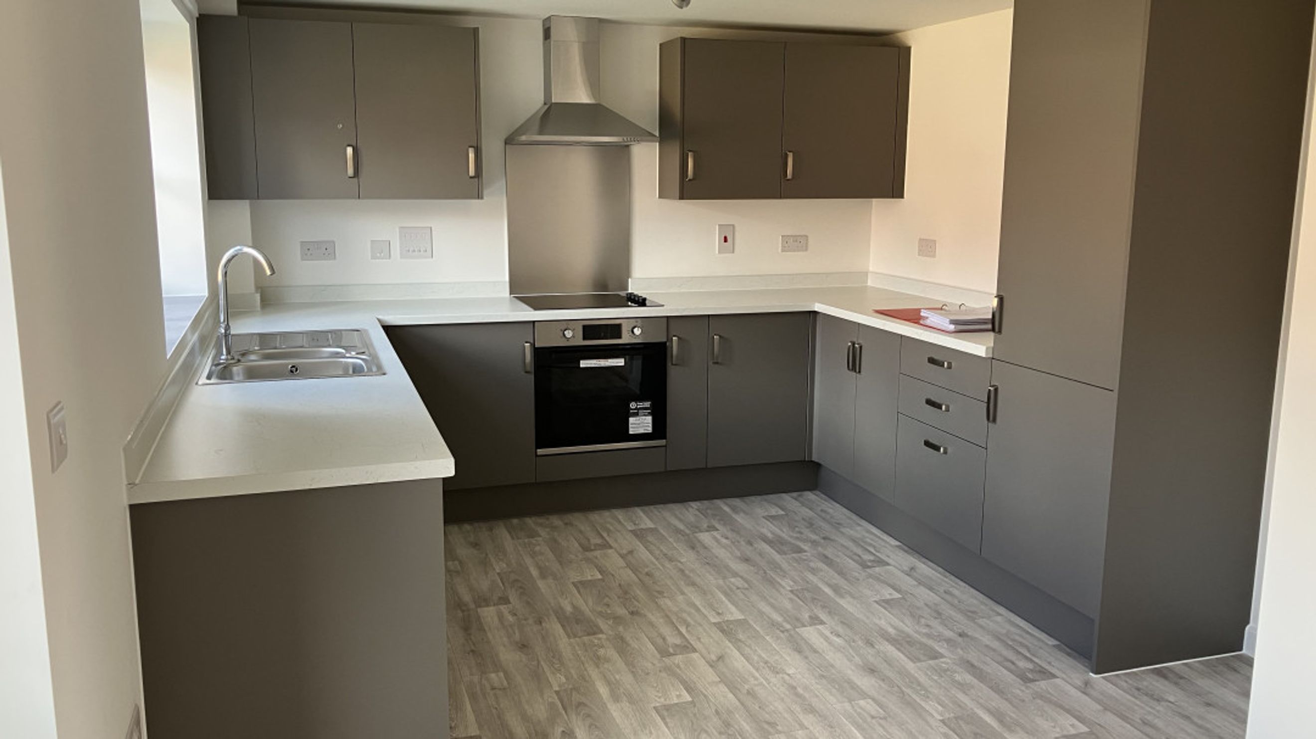 A modern kitchen with grey cabinets, a sink, an oven, and a stovetop.