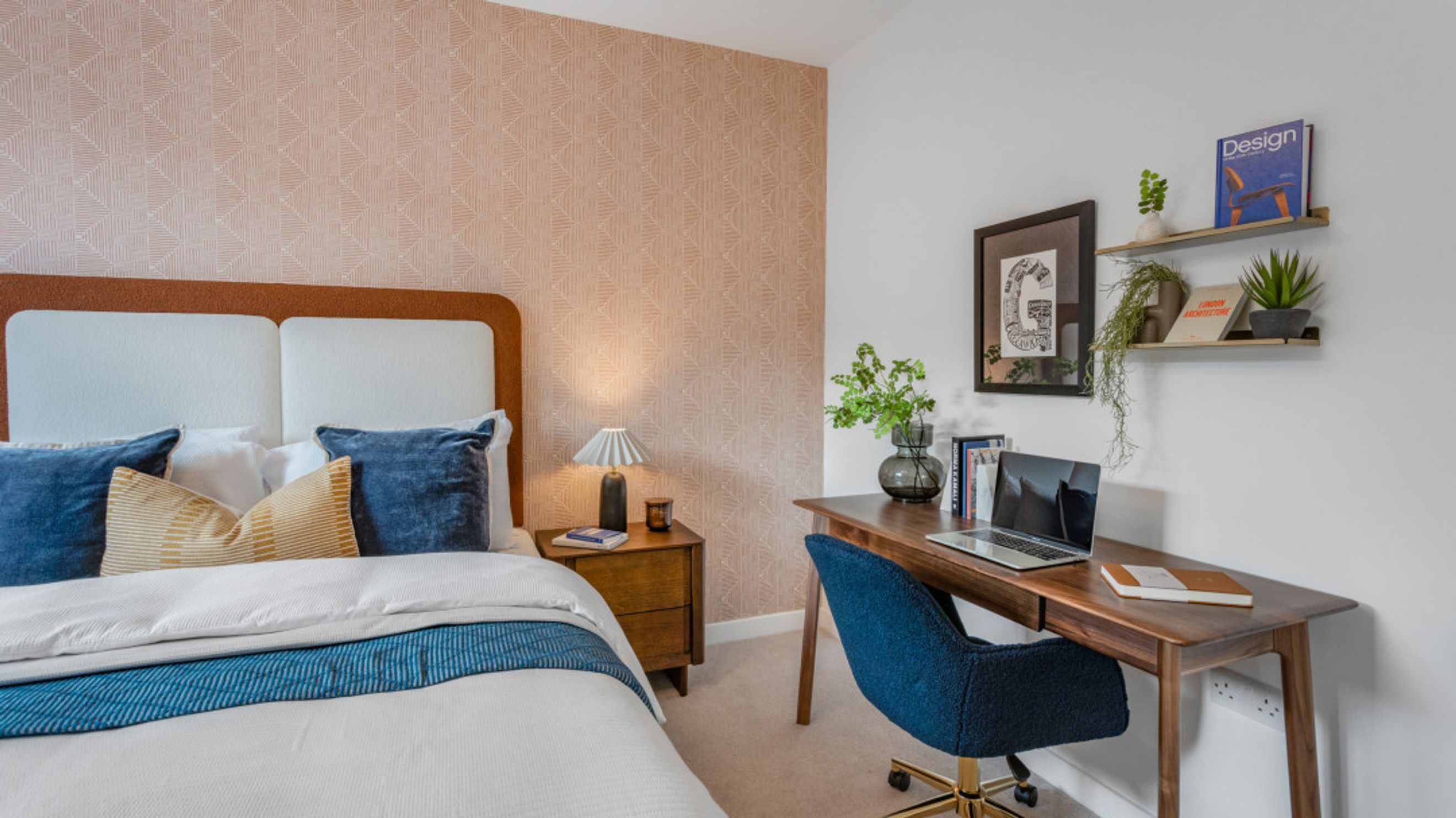 A bedroom with a bed, pillows, a bedside table with a lamp, and a desk with a chair and shelves.