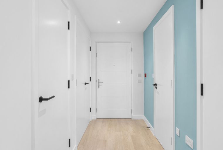 A hallway with multiple white doors and light wood flooring.