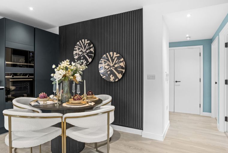 A dining area with a round table, chairs, and a slatted wall with artwork.