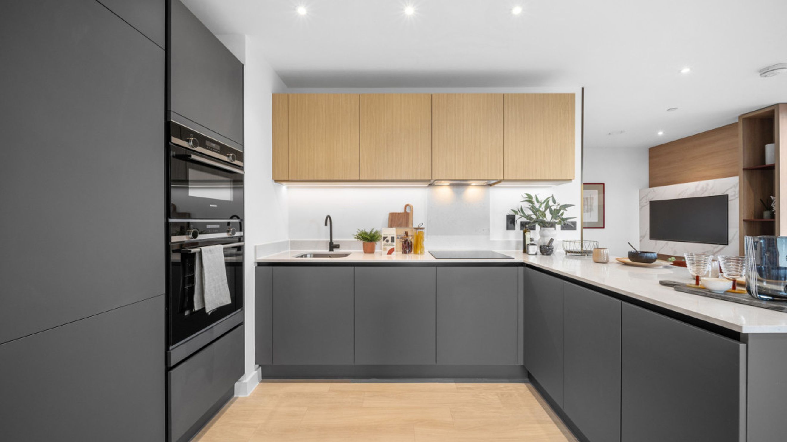 A modern kitchen with dark grey cabinets, wood overhead cabinets, and integrated appliances.