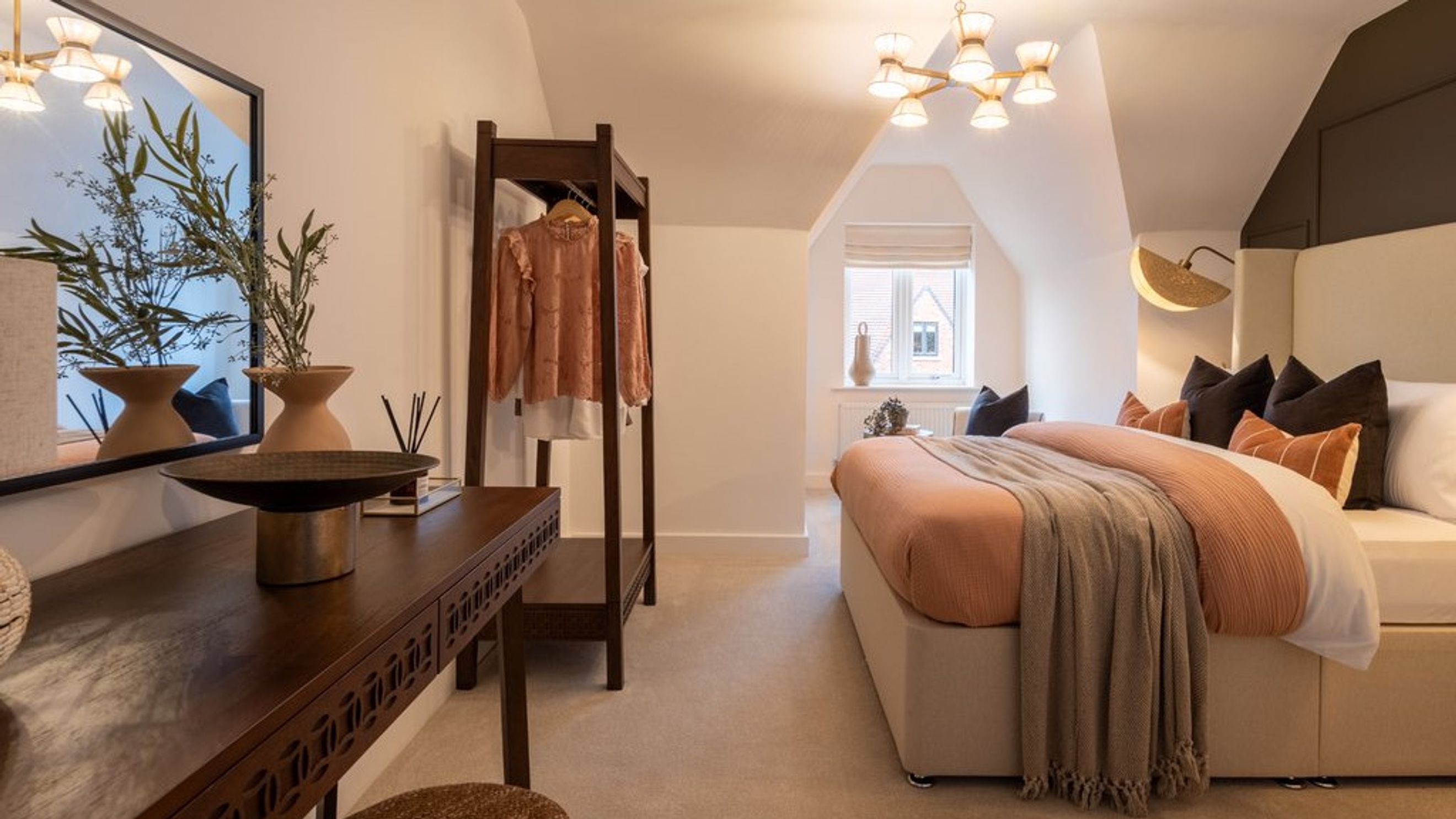 A bedroom with a bed, pillows, a throw blanket, an open wardrobe, and a vanity table.