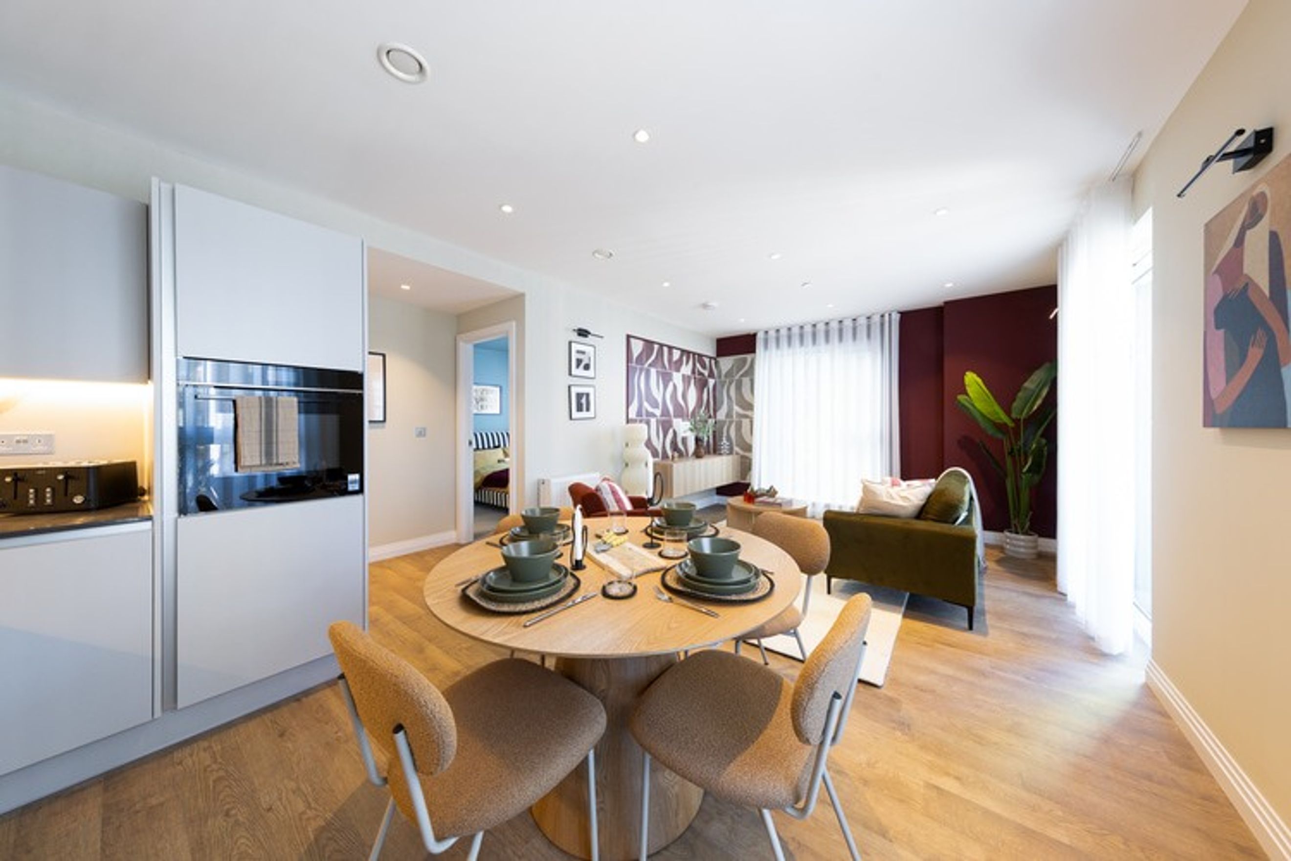 A dining area with a round table and chairs, adjacent to a living area with a sofa and a plant.