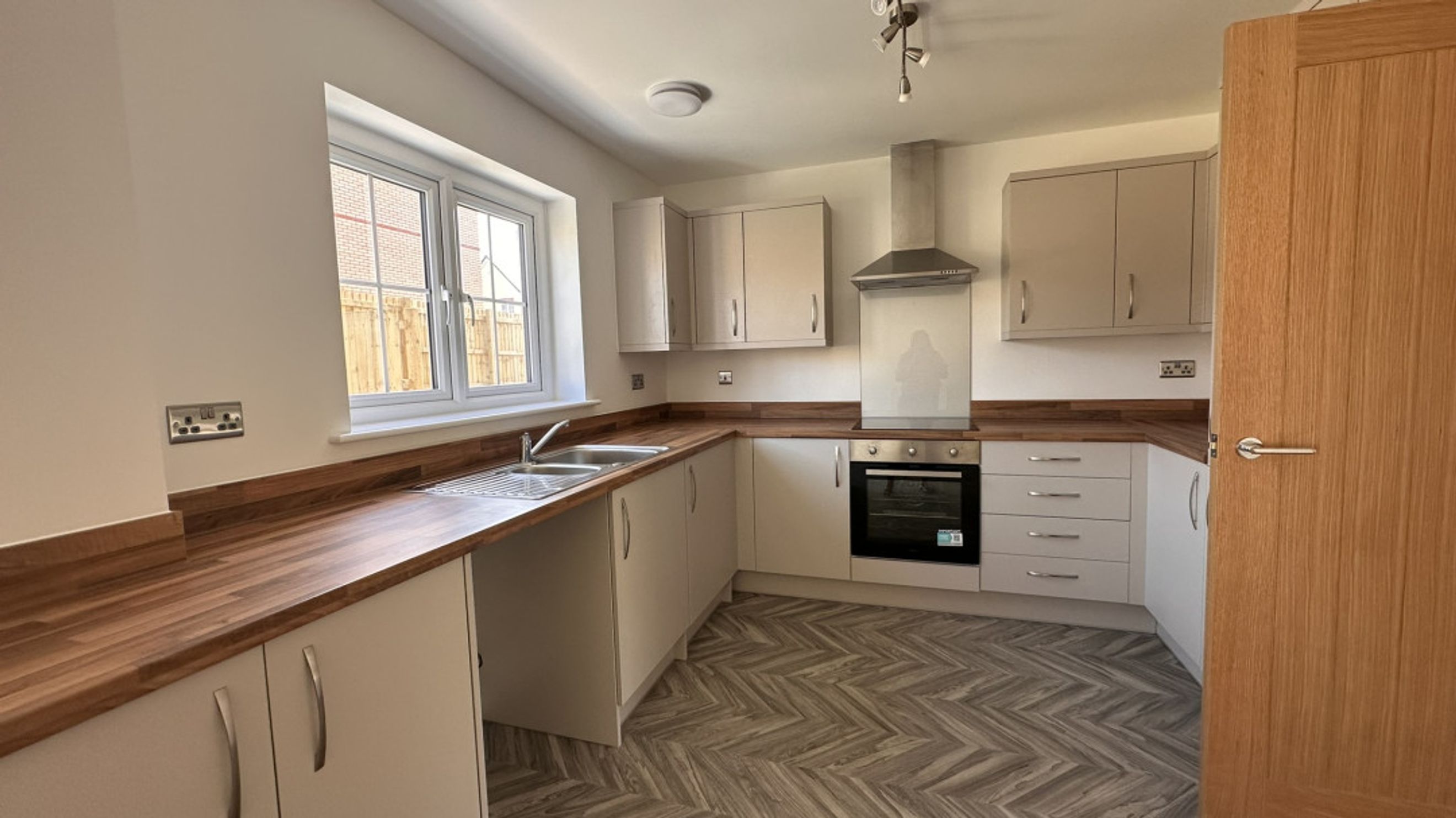 A kitchen with light-colored cabinets, wooden countertops, a sink, an oven, and a window.