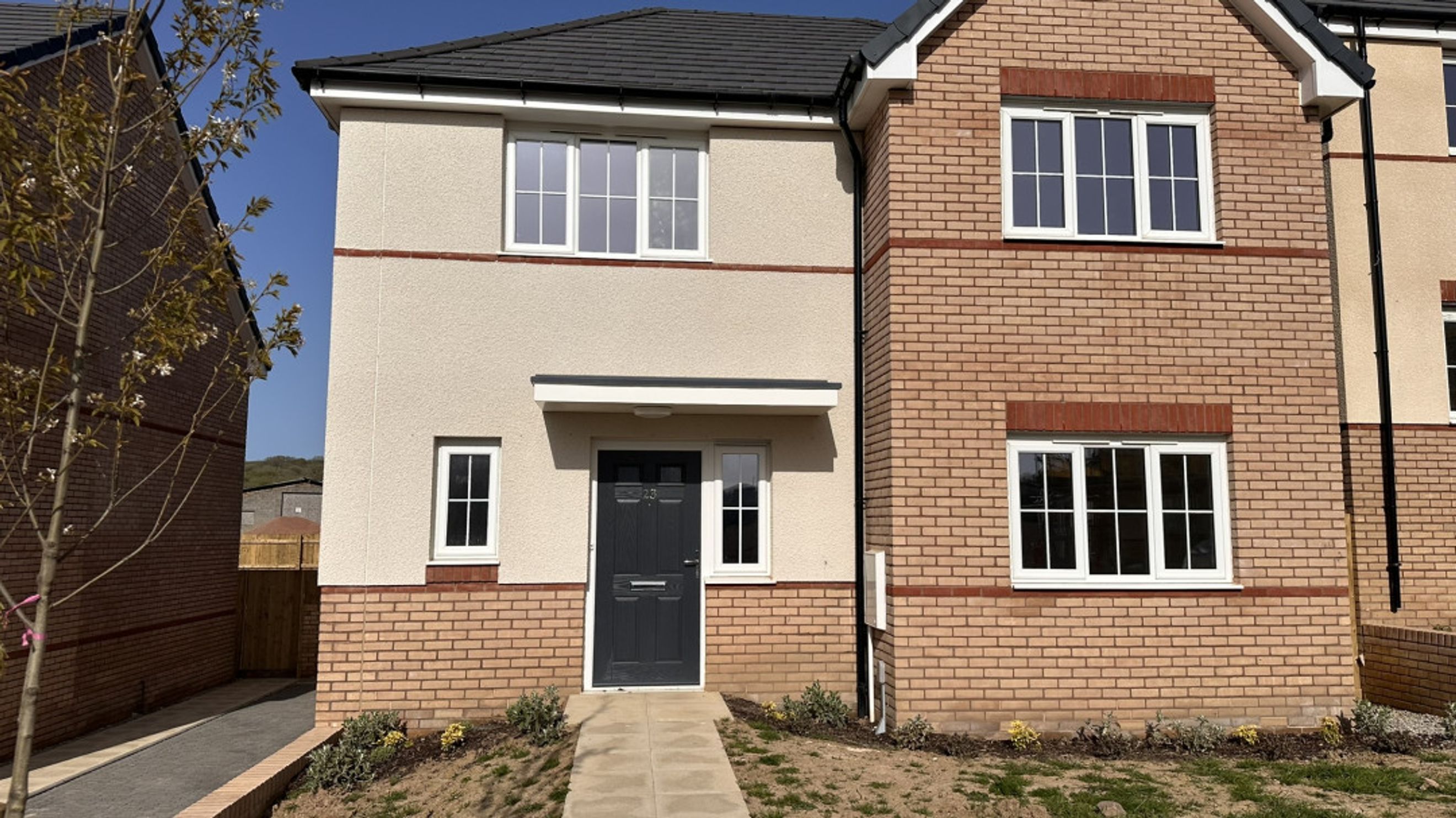 A new construction house with brick and stucco exterior, featuring multiple windows and a dark front door.