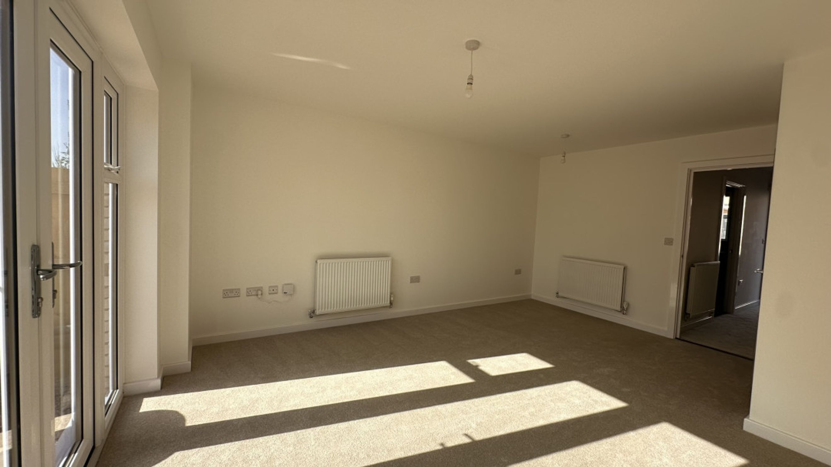 A spacious, unfurnished room with carpeted floors, white walls, and large glass doors.