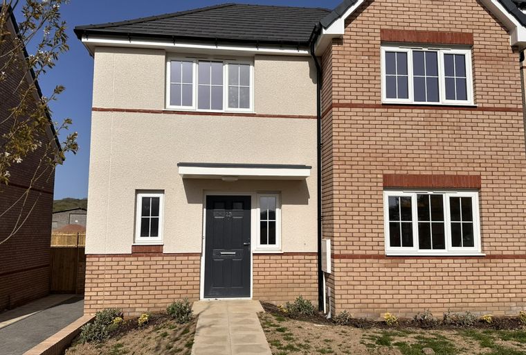 A new construction house with brick and stucco exterior, featuring multiple windows and a dark front door.
