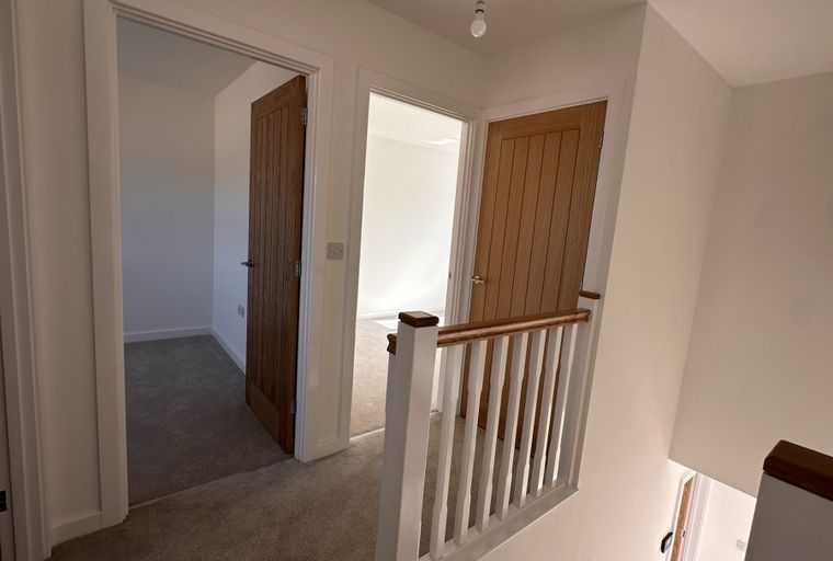 A hallway with two oak doors and a white banister.