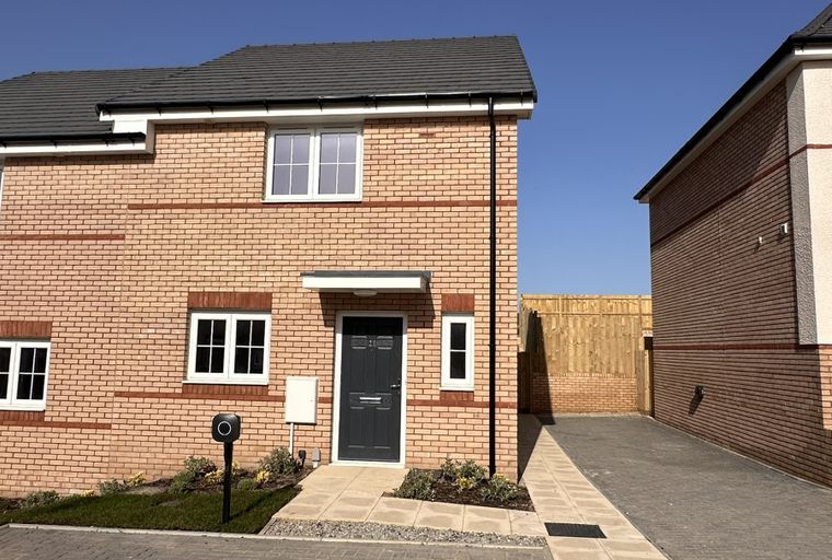A new build house with a brick facade, dark grey front door, and white-framed windows.