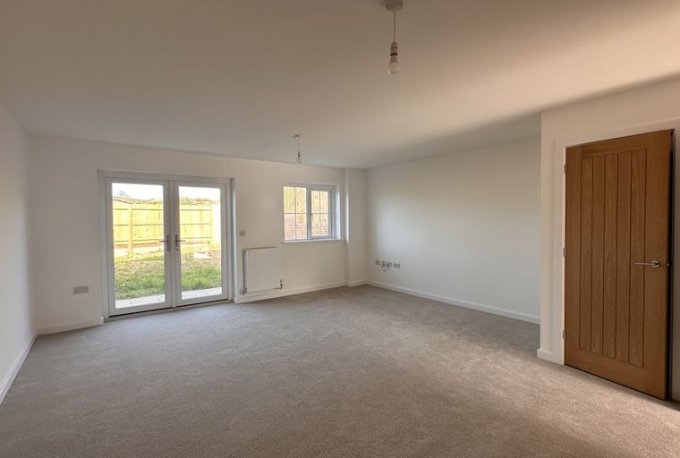 A living room with double doors, a window, a radiator, and two wooden doors.