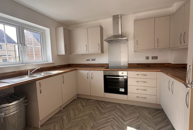 A modern kitchen with light-colored cabinets, a wooden countertop, a sink, and a built-in oven.