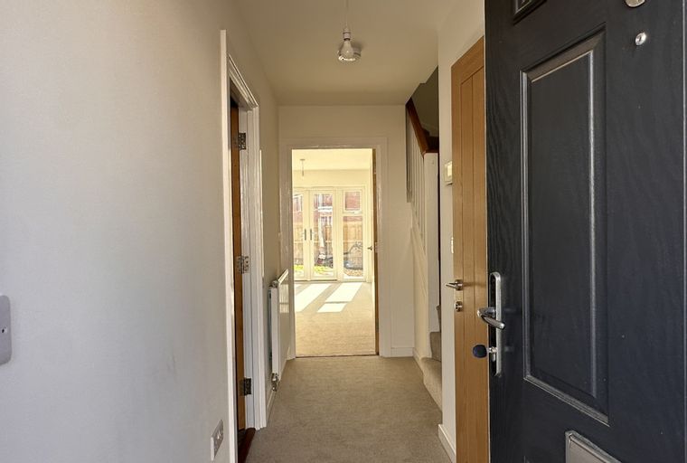 A hallway with a front door, a staircase, and double doors leading to a garden.