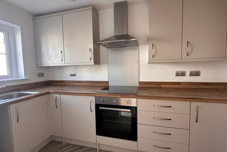 A kitchen with light-colored cabinets, a wooden countertop, a sink, an oven, and an extractor hood.