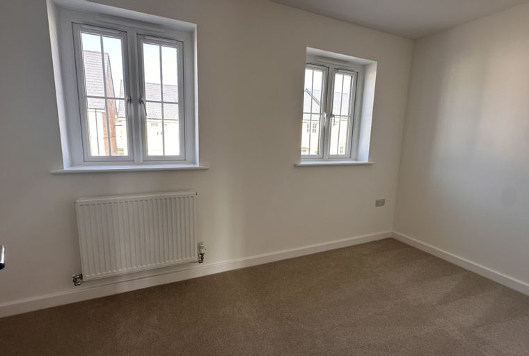 A room with two windows, a radiator, and a carpet.