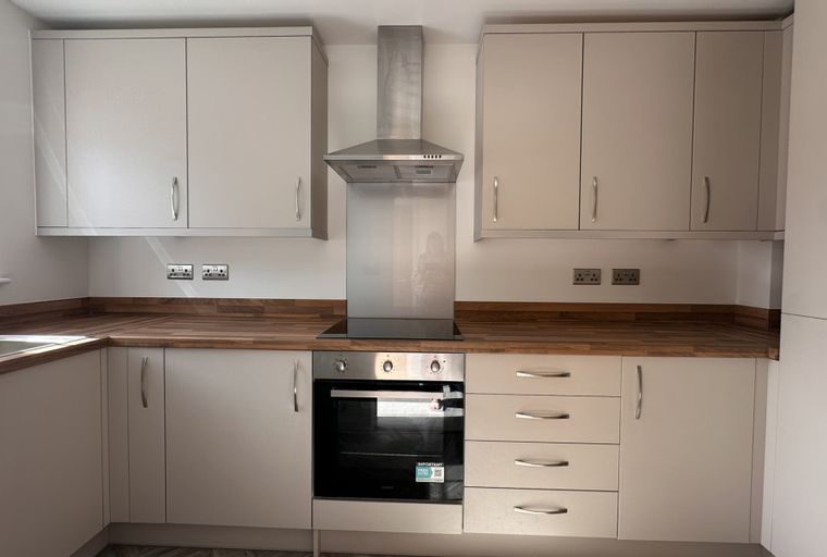 A modern kitchen with light-colored cabinets, a wooden countertop, and a stainless steel oven and range hood.