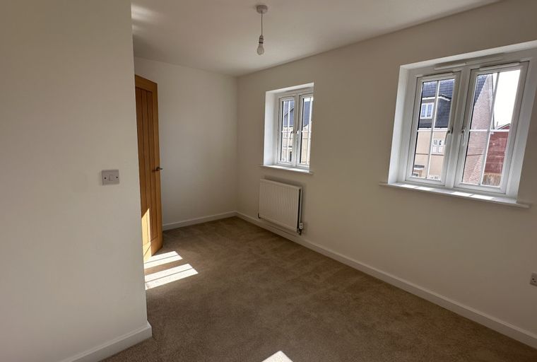 A bedroom with a wooden door, two windows, a radiator, and a light fixture.