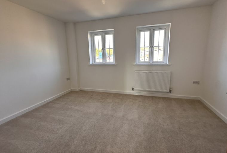 A bedroom with two windows, a radiator, and carpeted floors.
