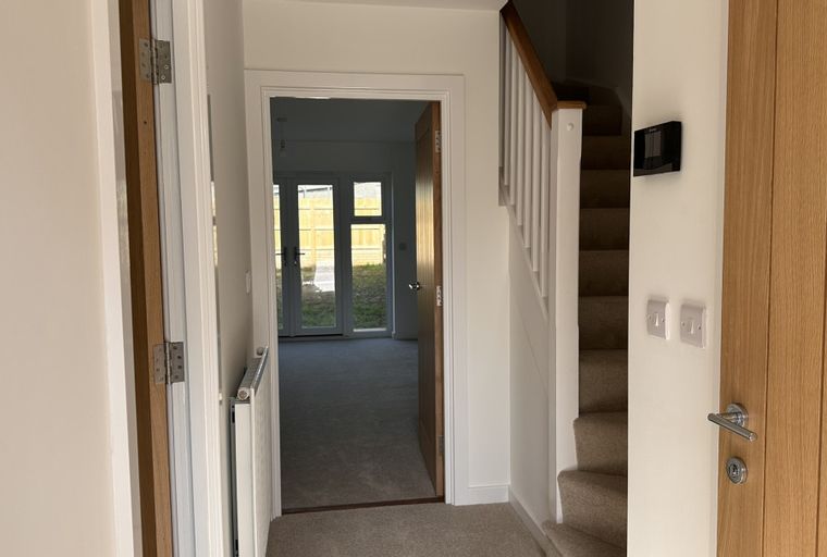 A hallway with a staircase, a wooden door, and a doorway leading to a living area.