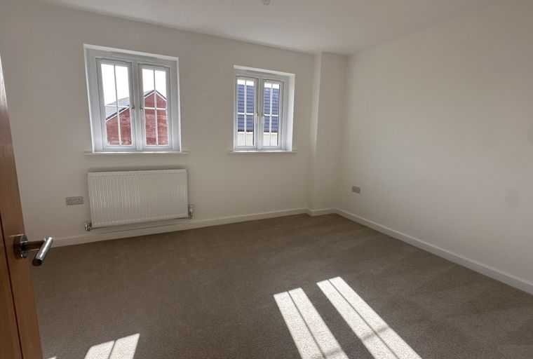 A bedroom with two windows, a radiator, and carpeted flooring.