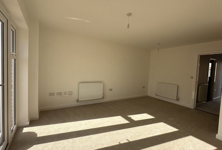 A spacious, unfurnished room with carpeted floors, white walls, and large glass doors.