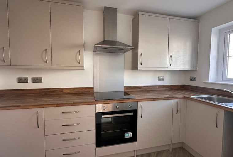 A kitchen with light-colored cabinets, wooden countertops, a sink, and an oven.