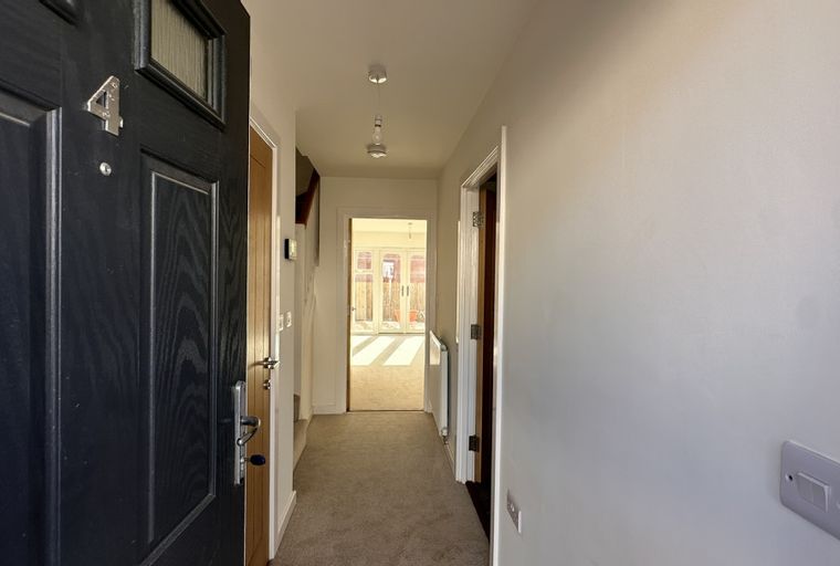 A hallway with a front door, interior doors, and a view into a living room with double doors.