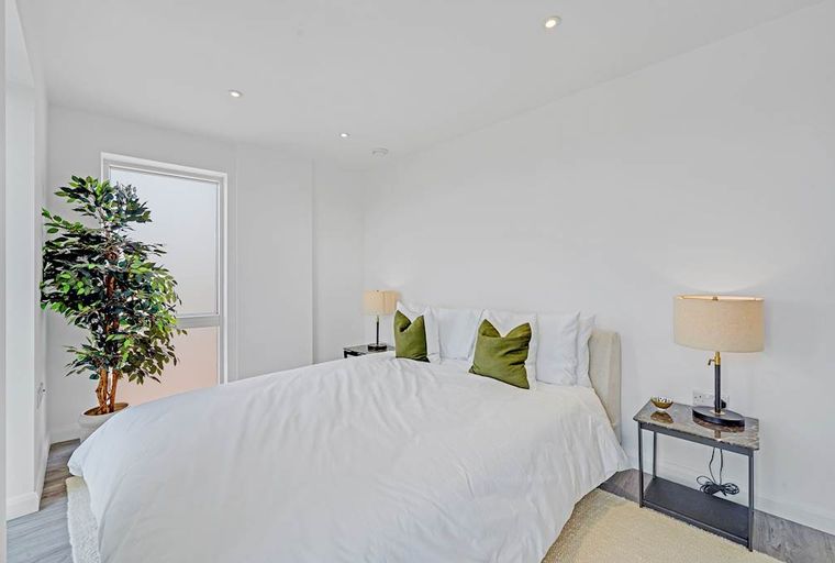 A bedroom with a bed, pillows, bedside tables, lamps, and a potted plant.