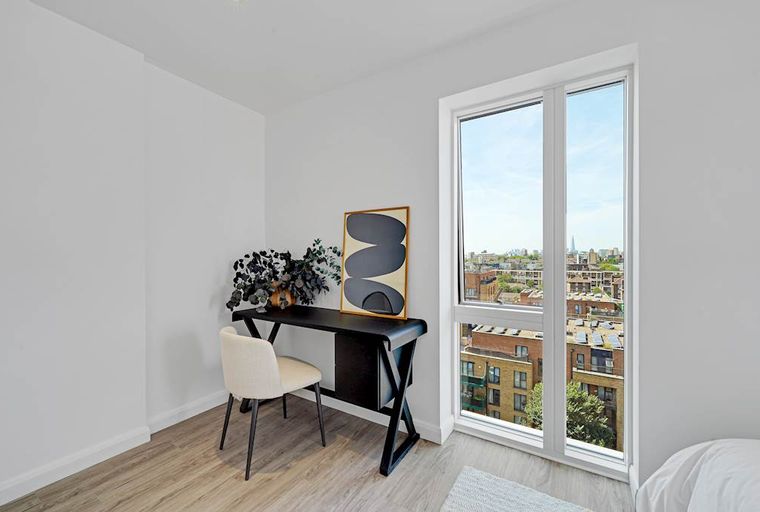 A desk with a chair and artwork in a room with a large window overlooking a city.