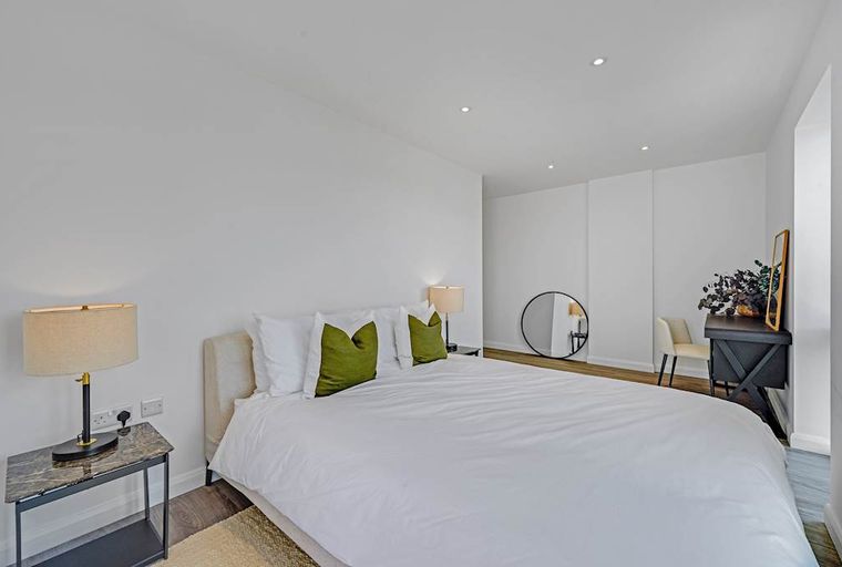 A bedroom with a bed, bedside tables, lamps, and a vanity.