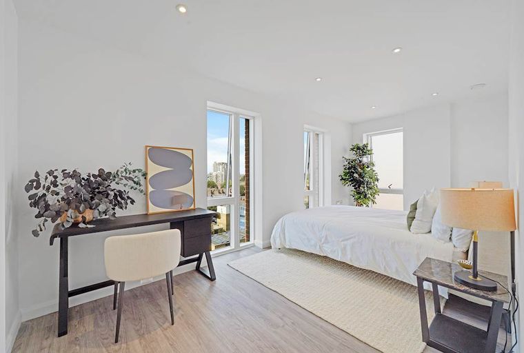 A bedroom with a bed, a desk, a chair, and a bedside table.