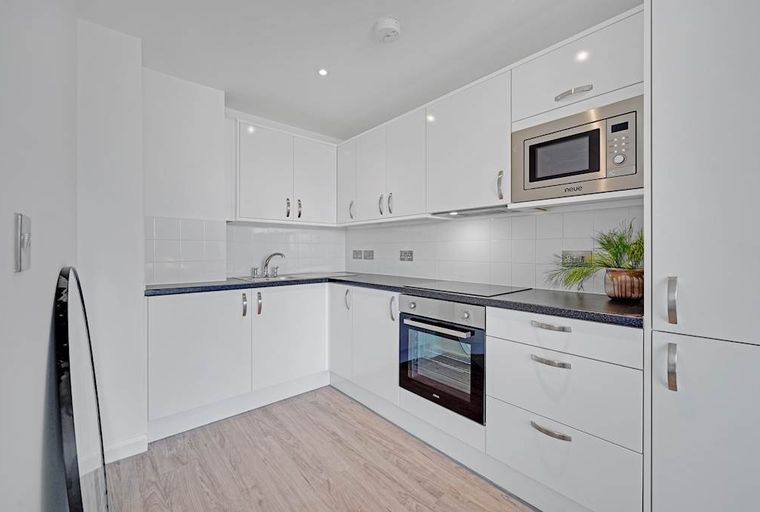 A modern kitchen with white cabinets, a dark countertop, an oven, and a microwave.