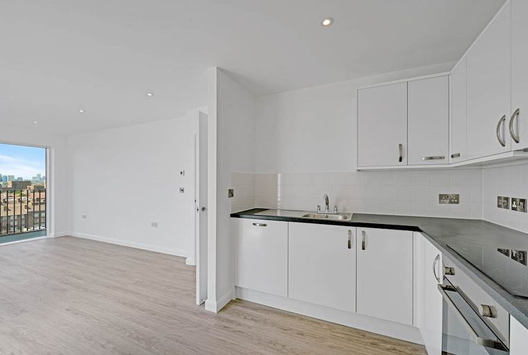 A modern kitchen and living area with white cabinets, a sink, and a balcony overlooking a city.