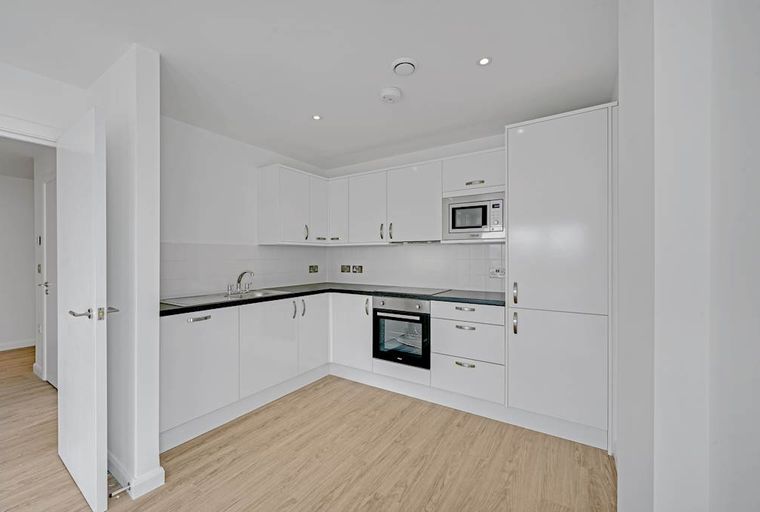 A modern kitchen with white cabinets, a sink, an oven, and a microwave.