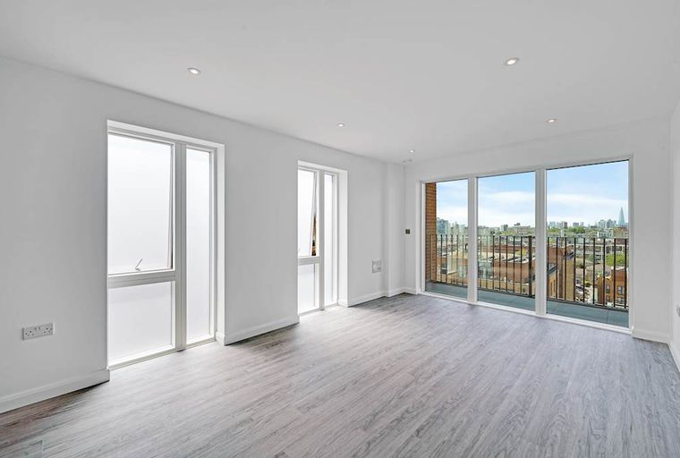A spacious, empty room with large windows and a balcony overlooking a city.