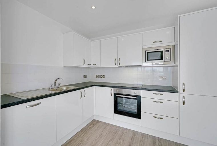 A kitchen with white cabinets, a black countertop, a sink, an oven, and a microwave.
