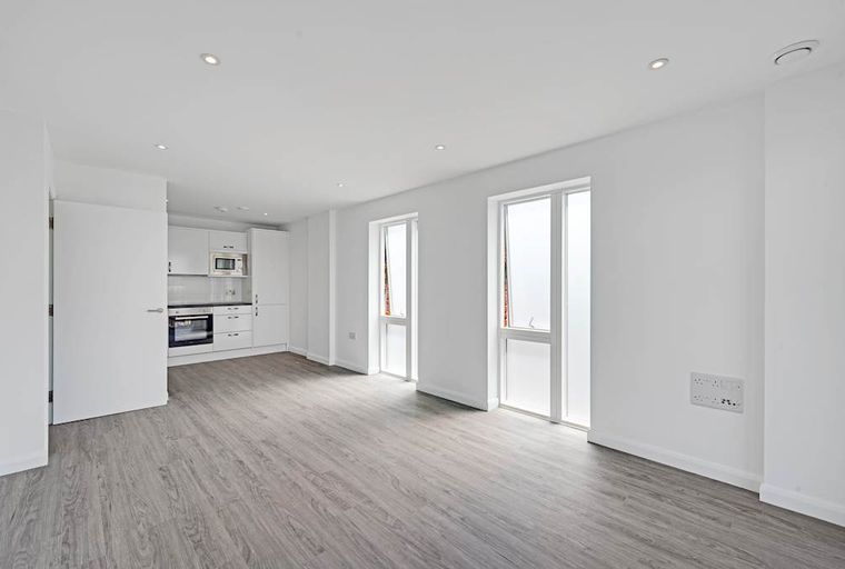 A modern, unfurnished studio apartment with a kitchen area and two large windows.