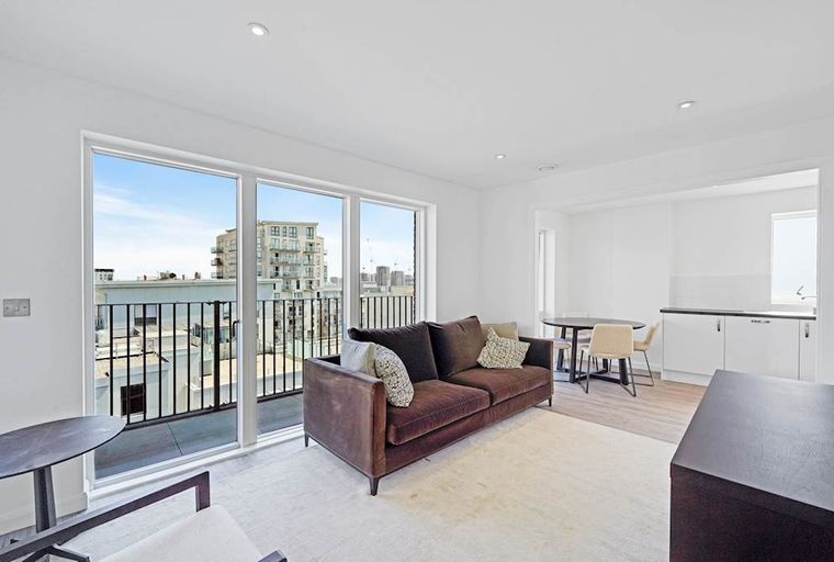 A living room with a sofa, balcony, dining area, and kitchen.